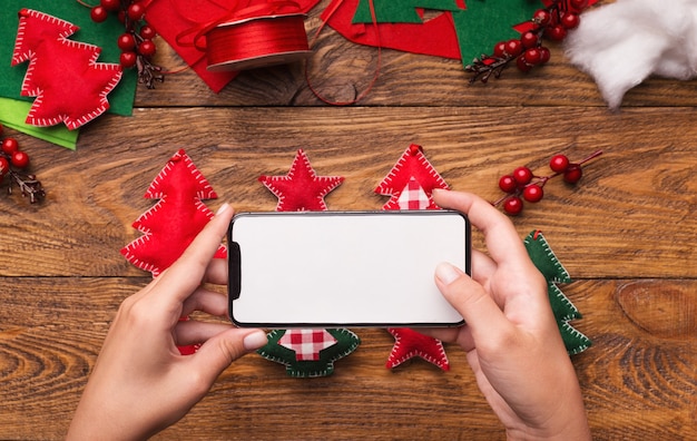 Redes sociais. Mãos de mulher tirando fotos de decorações de Natal feitas à mão por smartphone, tela em branco do celular para maquete, espaço de cópia