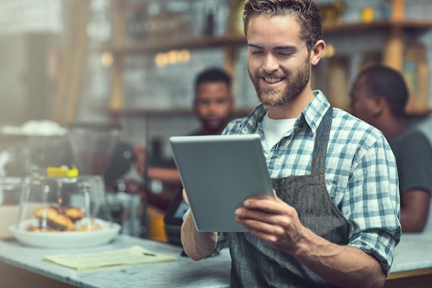 Foto las redes sociales son excelentes para aumentar la visibilidad de las pequeñas empresas fotografía de un joven usando una tableta digital en la tienda en la que trabaja