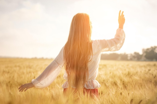 Redhaired Mädchen in einem Weizenfeld bei Sonnenuntergang Schöne Frau im goldenen Feld bei Sonnenuntergang Hintergrundbeleuchtete warme Töne