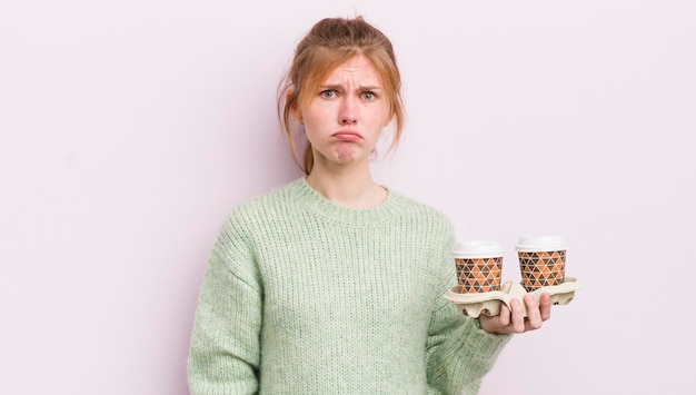 Redhead hübsches Mädchen fühlt sich traurig und weinerlich mit einem unglücklichen Blick und weint Kaffee zum Mitnehmen Konzept