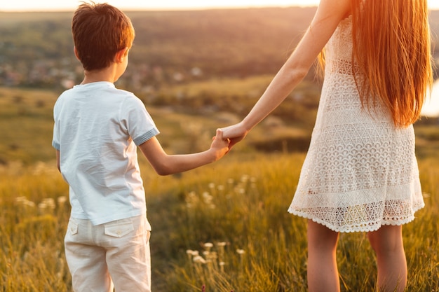 Redhead Teen Girl und kleiner Junge Händchenhalten bei Sonnenuntergang