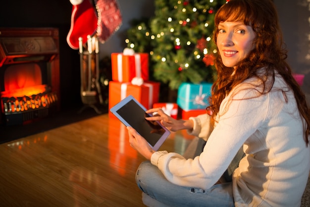 Redheadfrau, die auf Fußboden unter Verwendung der Tablette am Weihnachten sitzt