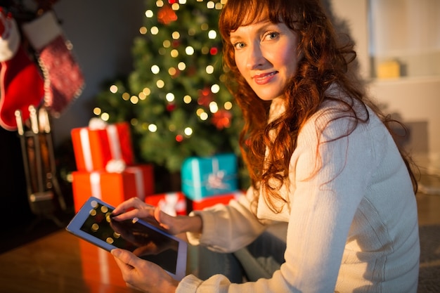 Redheadfrau, die auf Fußboden unter Verwendung der Tablette am Weihnachten sitzt