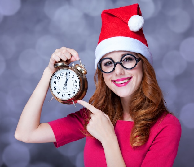 Redheadmädchen im Weihnachtshut mit Uhr