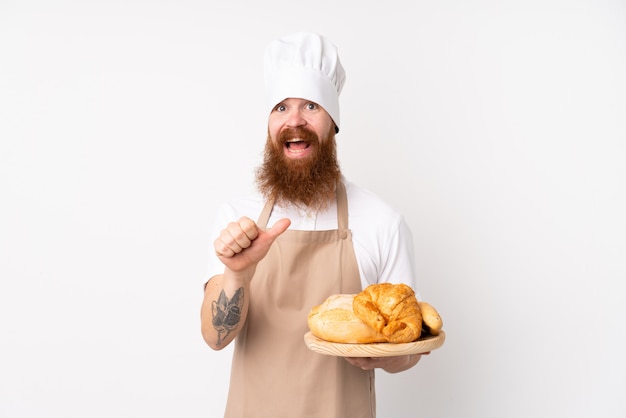 Redheadmann in der Chefuniform. Männlicher Bäcker, der eine Tabelle mit einigen Broten zeigen auf die Seite hält, um ein Produkt darzustellen