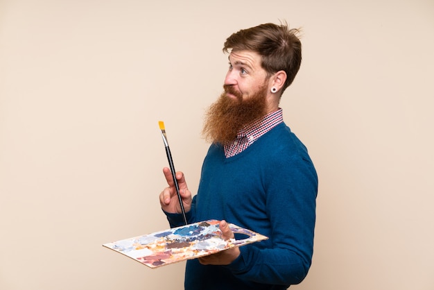 Redheadmann mit dem langen Bart, der eine Palette anhält und eine Idee denkt