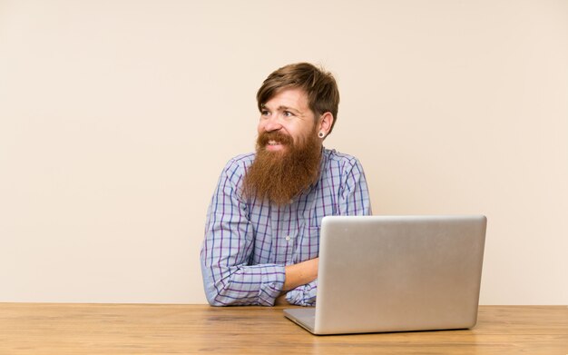 Redheadmann mit langem bart in einer tabelle mit einem laptoplachen