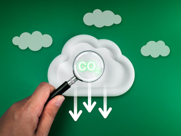 Reduzieren Sie die CO2-Emissionen, um den Klimawandel und die globale Erwärmung zu begrenzen. Konzept der Netto-Null-Kohlenstoffdioxid-Reduktion CO2-Symbol konzentriert sich in einer Lupe auf weiße Wolke mit Pfeilzeichen nach unten, grünen Hintergrund