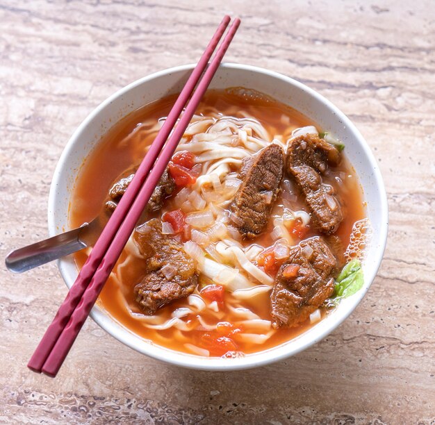 Refeição de macarrão de carne com caldo de molho de tomate em tigela na mesa de madeira brilhante famosa comida de estilo chinês em Taiwan close-up vista superior cópia espaço