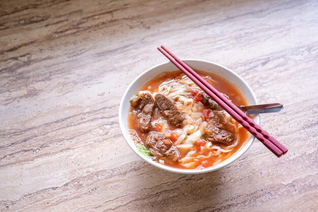 Refeição de macarrão de carne com caldo de molho de tomate em tigela na mesa de madeira brilhante famosa comida de estilo chinês em Taiwan close-up vista superior cópia espaço