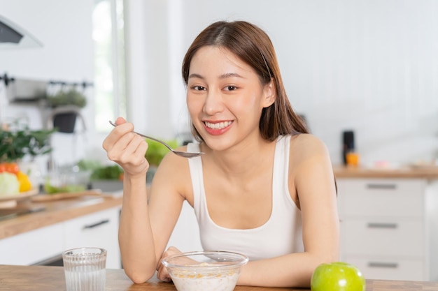 Refeição feliz de menina bonita comendo café da manhã saudável na manhã jovem asiática tendo cereais granola com leite fresco na tigela na cozinha Dieta conceito de pessoas de comida vegetariana