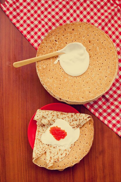 Refeição festiva do entrudo Maslenitsa. Blini de panqueca russa com creme fresco e caviar vermelho na parede de madeira