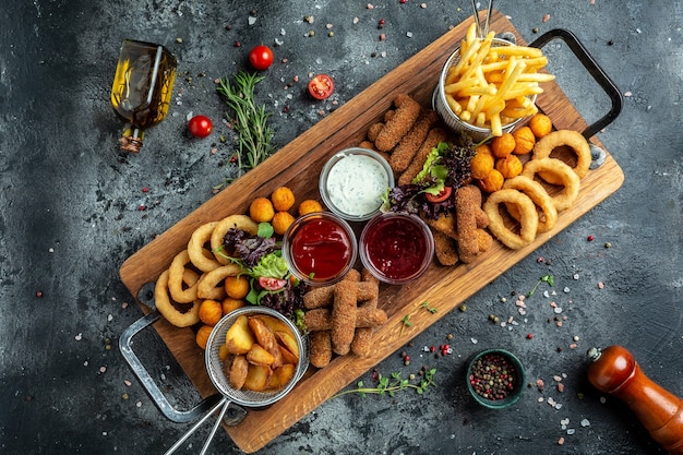 Refeições fast food em palitos de mussarela, rodelas de cebola, batata frita, nuggets de frango e molho. aperitivos de pub em uma placa de madeira. banner, menu, local de receita para texto, vista superior.