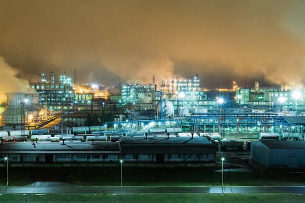 Refinería de petróleo con tuberías y complejos de destilación durante la noche.