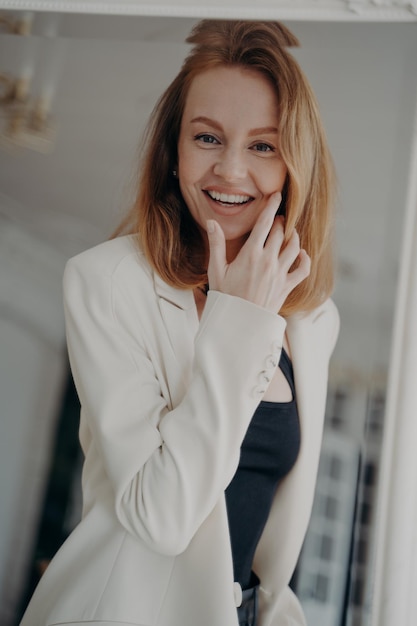 Reflejo de espejo de una emocionada mujer rubia adulta eligiendo un traje de moda