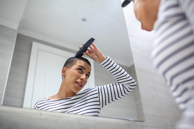 Reflejo de espejo de mujer de pelo corto en la parte superior del tanque con máquina de corte de pelo