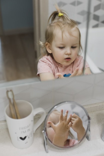 Reflejo en el espejo de una niña divertida lavándose las manos y la cara en el baño