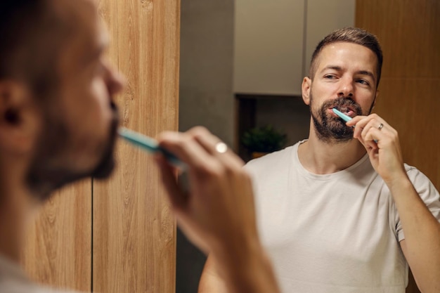 Reflejo de un hombre cepillándose los dientes en un baño.