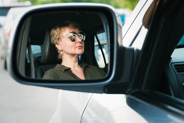 Reflejo de una mujer de mediana edad conduciendo un auto en el espejo lateral del auto