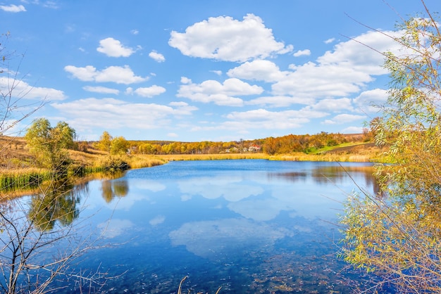 Reflejo de nubes en un río tranquilo en el campo de otoño