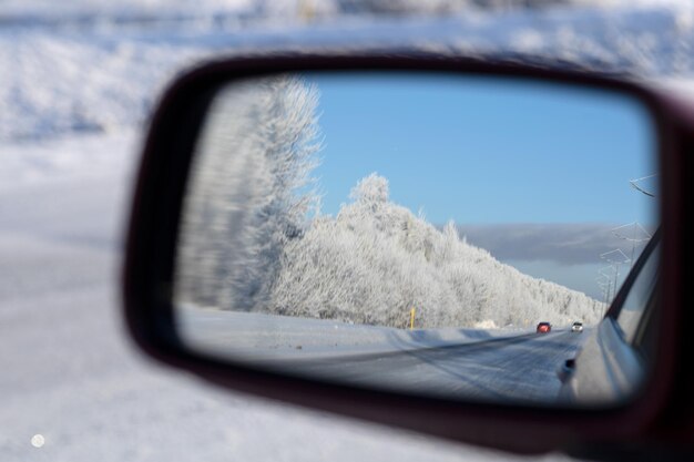 Reflexão da paisagem florestal e da estrada coberta de neve no espelho retrovisor do carro num dia gelado de inverno