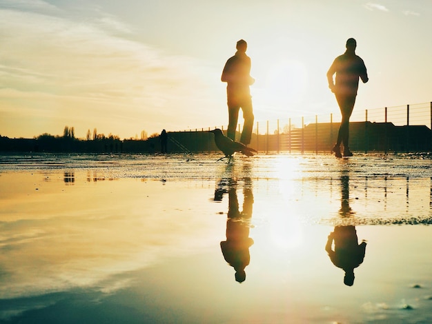 Reflexão de pessoas na poça enquanto correm durante o pôr do sol
