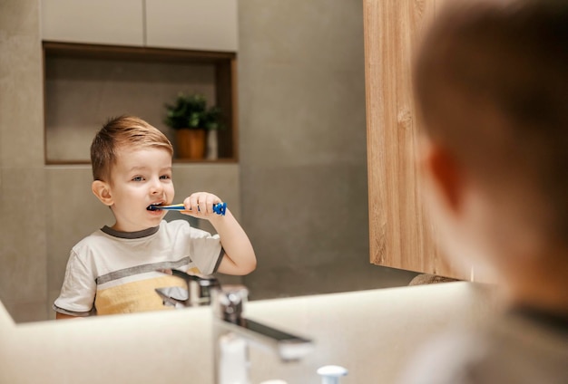 Reflexão de um garotinho parado no banheiro e escovando os dentes