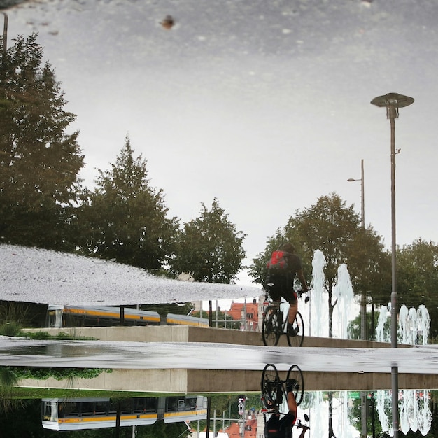 Reflexão de um homem andando de bicicleta em uma poça na rua