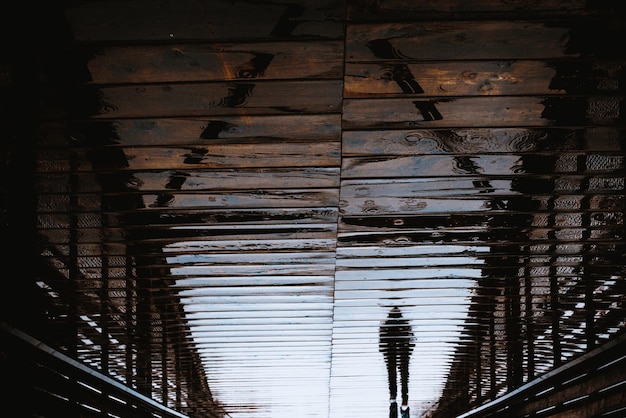 Foto reflexão de um homem andando em uma ponte de madeira