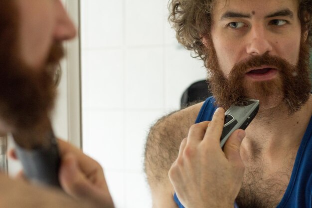 Foto reflexão de um homem cortando a barba no espelho do banheiro