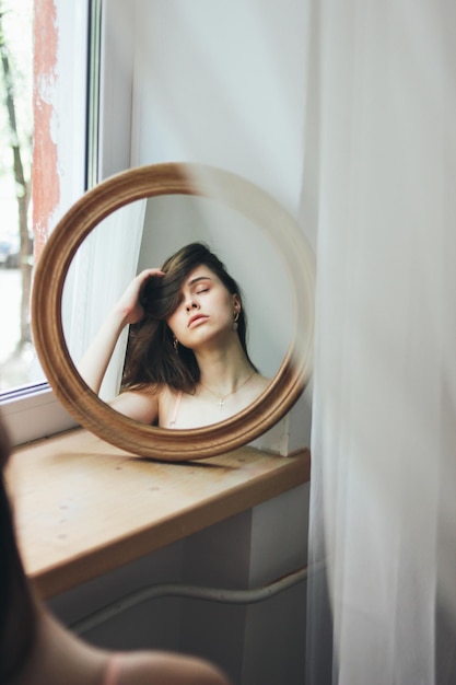 Reflexão de uma mulher bonita e cansada no espelho circular em casa.