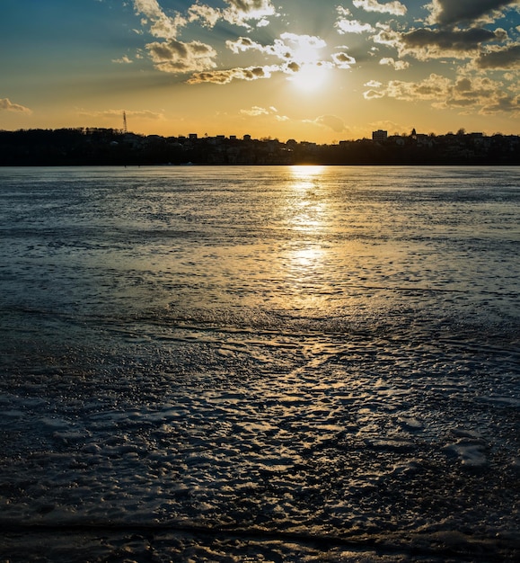 Reflexão do pôr do sol no gelo rachado congelado no degelo a silhueta da costa