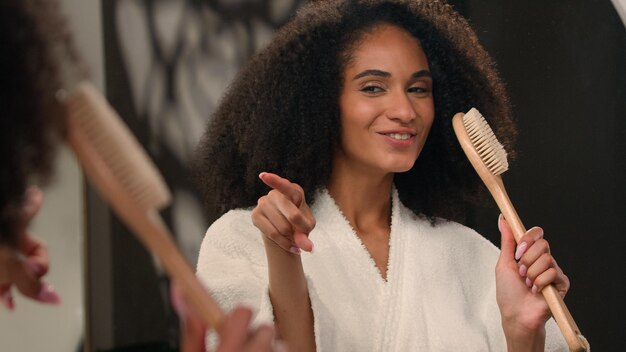 Foto reflexão feminina de perto cantando feliz despreocupada mulher afro-americana alegre cantando em escova de banho