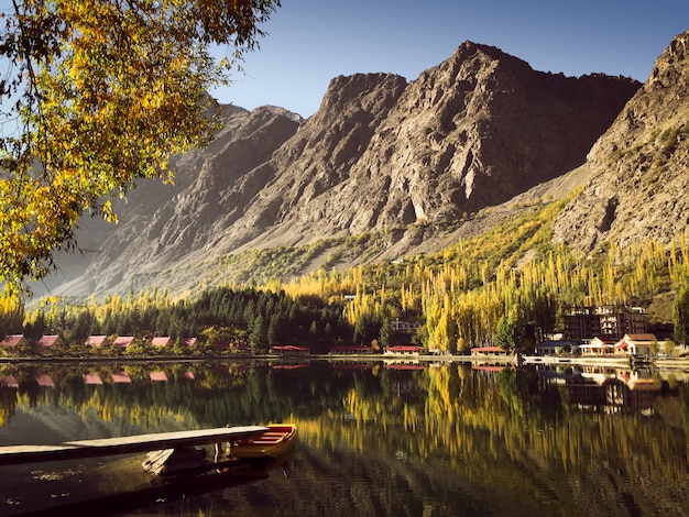 Reflexión en el agua de la montaña y árboles coloridos en otoño con un barco atracado en el lago.