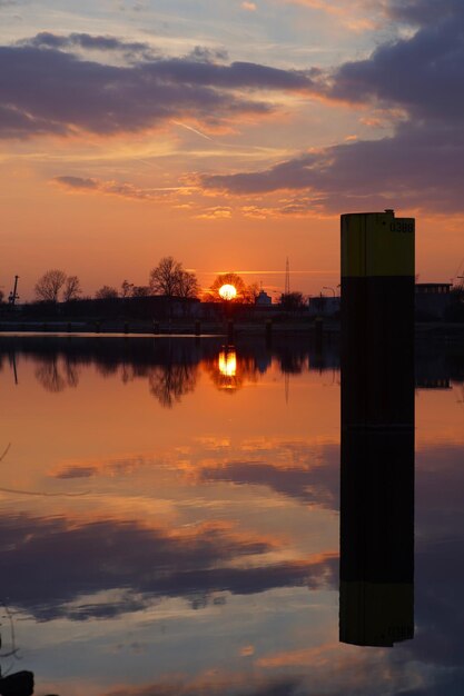 Foto reflexión de árboles de silueta en el agua contra el cielo naranja.