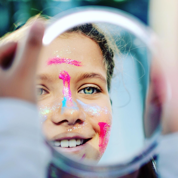 Foto reflexión de una chica con la cara pintada sonriendo en el espejo