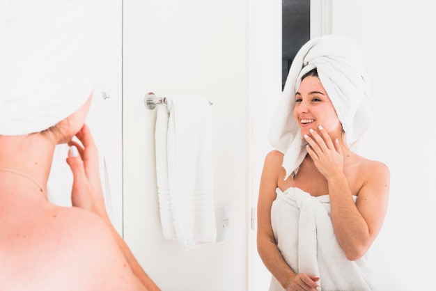 Reflexion der schönen Frau schauend im Bademantel mit einem Tuch auf ihrem Kopf