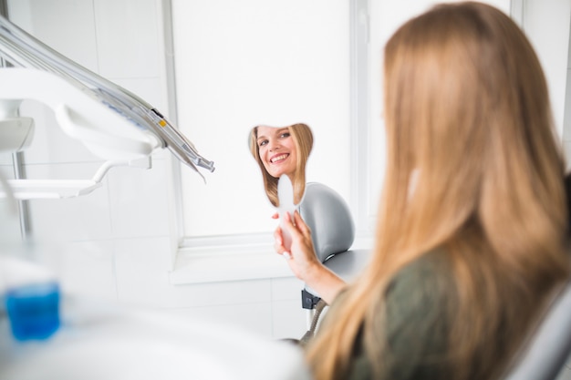 Reflexion des lächelnden Spiegels der jungen Frau in der Hand an der Klinik