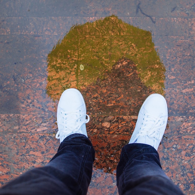 Reflexion des Mannes mit gelbem Regenschirm in weißen Turnschuhen in Pfütze