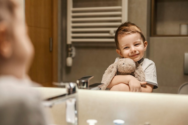 Reflexion eines kleinen Jungen, der sich im Spiegel betrachtet, während er Häschen umarmt