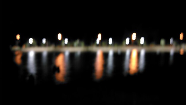 Reflexión de los equipos de iluminación iluminados en el lago contra un cielo despejado