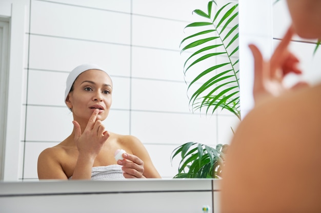 Reflexion im Spiegel einer Frau, die den hygienischen Lippenstift einer Frau mit einem Finger auf ihren Lippen trägt