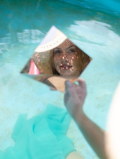 Foto reflexión de una mujer en el espejo mientras está sentada en la piscina