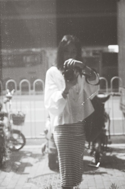 Foto reflexión de una mujer fotografiando con una cámara en una ventana de vidrio