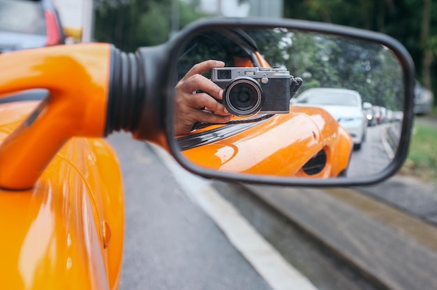 Foto reflexión de una persona en el espejo lateral mientras se toma una fotografía en un automóvil con una cámara