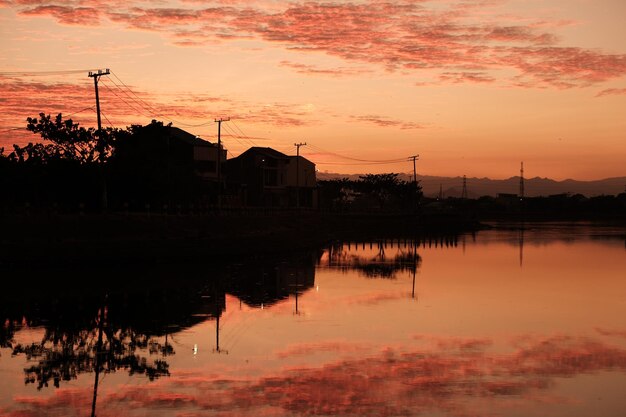 Reflexión de las siluetas de los árboles en el lago contra el cielo naranja