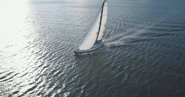 Foto reflexión del sol en primer plano yate de lujo en la bahía del océano aérea velas blancas del viento en el barco de pasajeros