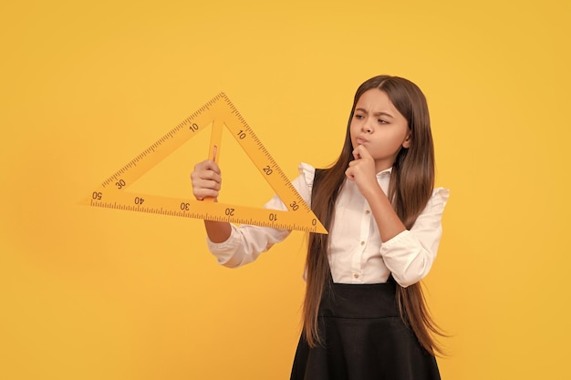 Reflexionando sobre el niño en el uniforme escolar sostenga el triángulo matemático para medir las matemáticas