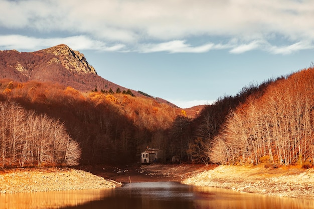 Reflexiones del bosque de otoño en el lago bajo un cielo nublado y una cabaña junto a la orilla del lago