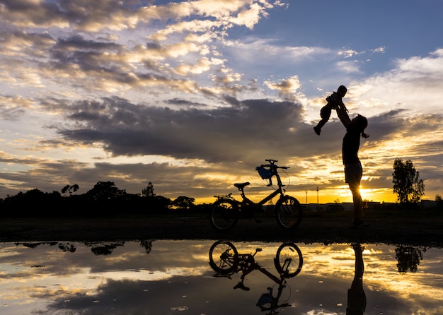 Reflexions-Schattenbild der Mutter mit ihrem Kleinkind gegen den Sonnenuntergang.